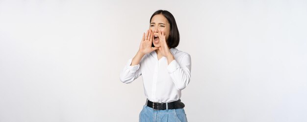 Image d'une jeune femme asiatique appelant quelqu'un criant fort et cherchant autour debout contre w