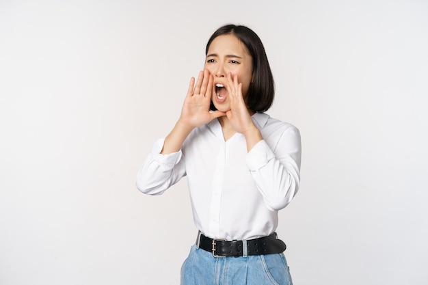 Image d'une jeune femme asiatique appelant quelqu'un criant fort et cherchant autour debout sur fond blanc