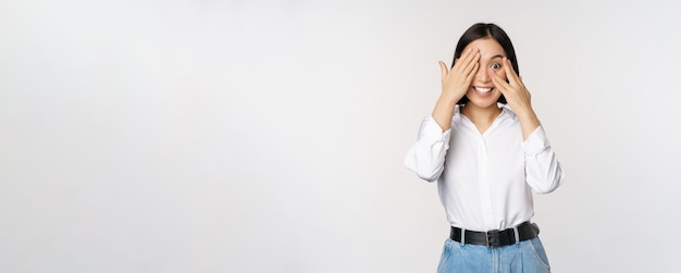 Image d'une jeune femme asiatique ferme les yeux et sourit attend la surprise anticipe jeter un coup d'œil à travers les doigts se dresse sur fond blanc