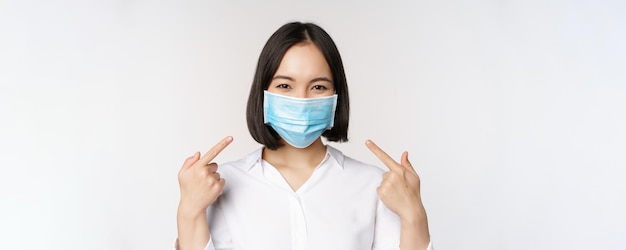 Image d'une jeune femme asiatique pointant vers elle-même tout en portant un masque médical concept de protection covid19 debout sur fond blanc