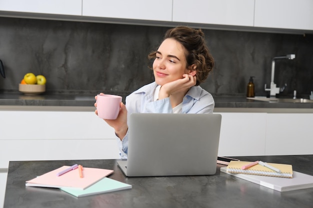 Photo gratuite image d'une jeune femme boit une tasse de café et travaille depuis une fille à la maison parcourant les boutiques de sites web en ligne sur