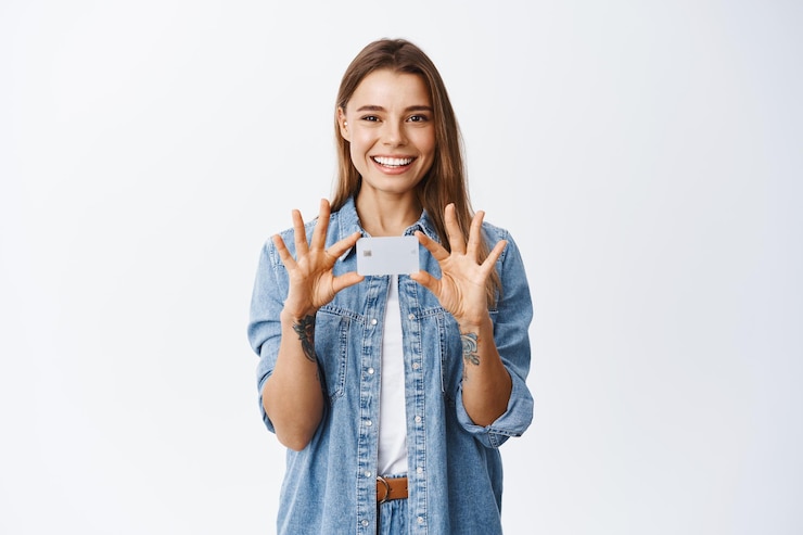 Photo gratuit image d'une jeune femme caucasienne souriante avec une émotion positive, montrant une carte de crédit en plastique sur la poitrine, recommande un dépôt bancaire, debout sur du blanc
