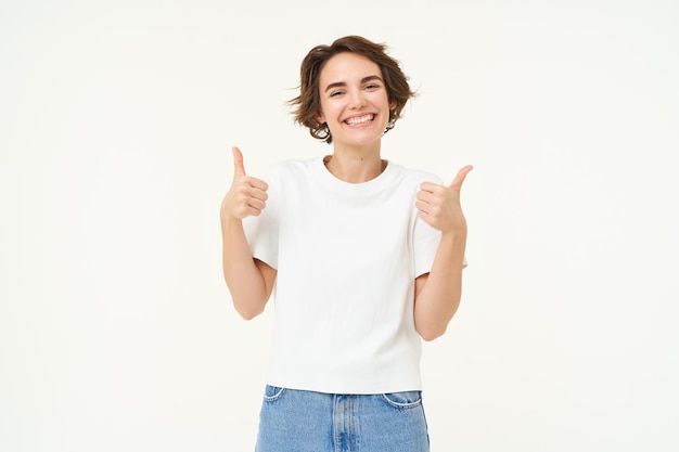 Photo gratuite l'image d'une jeune femme donnant des commentaires positifs montre les pouces vers le haut et les regards souriants en toute confiance