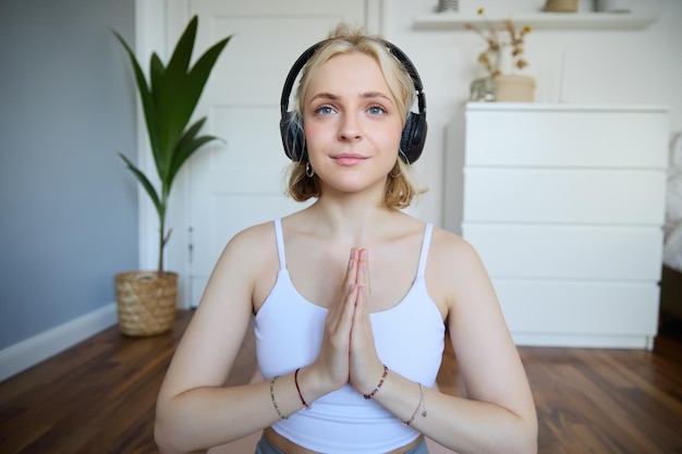 Photo gratuite image d'une jeune femme écoutant un podcast de yoga pour débutants, tenant les mains dans un signe de namaste.