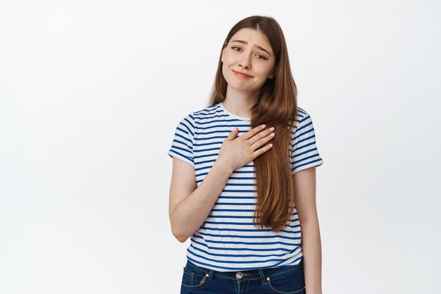 Image d'une jeune femme flattée tenir la main sur le cœur et avoir l'air reconnaissante sur le blanc