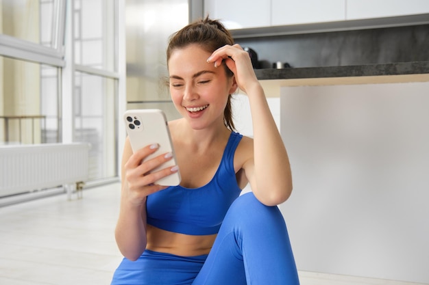 Photo gratuite image d'une jeune femme en forme portant un soutien-gorge sportif et des leggings bleus utilisant une application pour smartphone qui s'entraîne à partir de