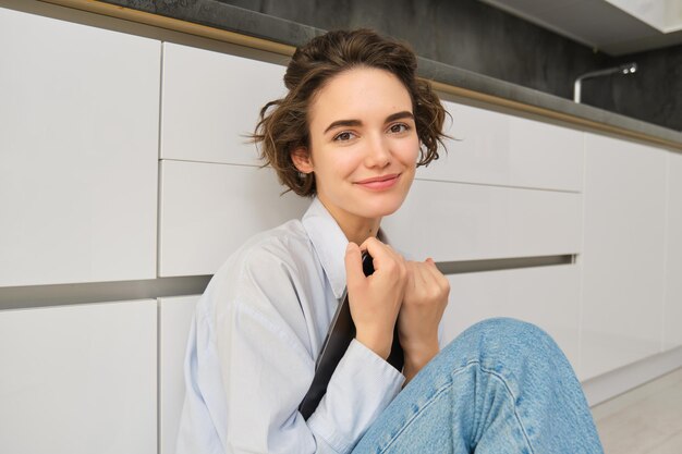 Image d'une jeune femme heureuse assise à la maison sur le sol tient une tablette numérique fait des achats en ligne en lisant e