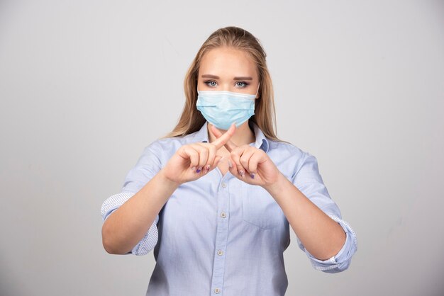 Image d'une jeune femme portant un masque médical montrant les doigts croisés