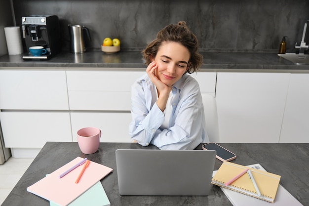 Photo gratuite image d'une jeune femme qui travaille regardant un ordinateur portable assise à la maison et regardant un webinaire se connectant à