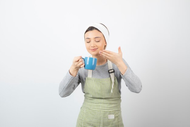 Image d'une jeune femme souriante en tablier pointant vers une tasse bleue