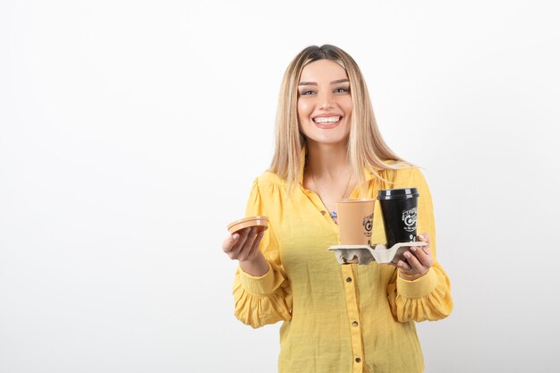 Image de jeune femme tenant des tasses de café en souriant.