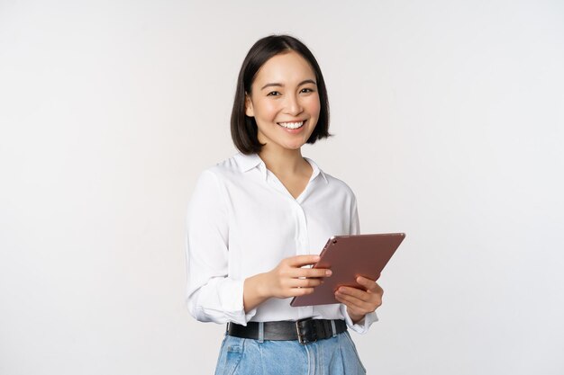 Image d'une jeune femme travaillante coréenne, directrice générale, tenant une tablette et souriant debout sur fond blanc