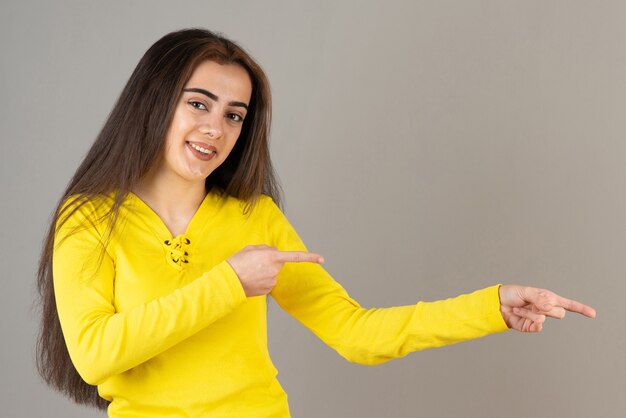 Image de jeune fille en haut jaune debout et posant sur un mur gris.