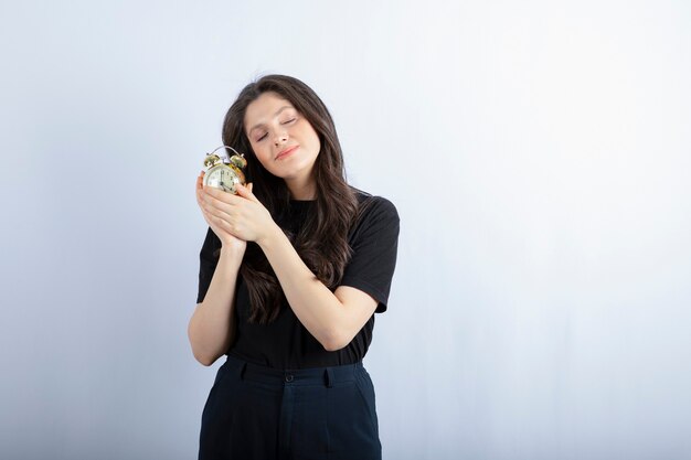 Image de jeune fille avec réveil dormant sur fond gris.