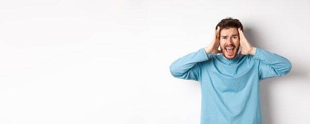 Photo gratuite image d'un jeune homme de race blanche criant de panique à la frustration et criant à l'appareil photo debout o