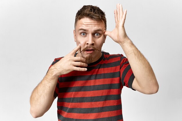 Image d'un jeune homme séduisant avec une moustache de guidon et une barbe de barbiche ayant un regard panique oublié, regardant la caméra avec la bouche ouverte, oublié de faire quelque chose de très important. Sentiments humains