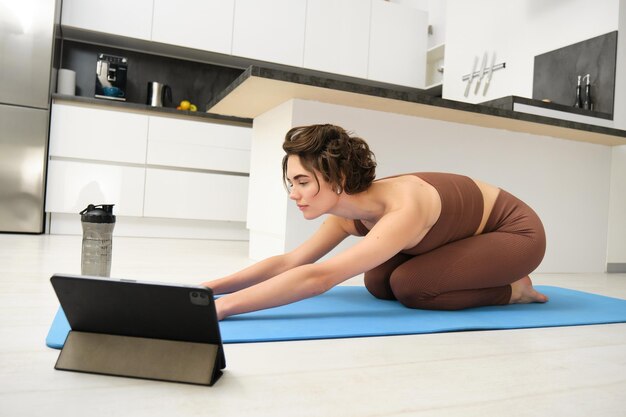 Photo gratuite image d'une jeune sportive faisant du yoga à la maison et regardant une vidéo de didacticiel d'instructeur de gym sur une tablette