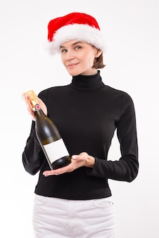 Image d'une jolie femme avec une coupe de champagne et une bouteille dans les mains. gants blancs. fond de studio clair. chapeau de père noël. technique mixte