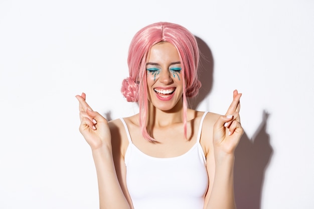 Image de jolie fille souriante faisant voeu avec les yeux fermés et les doigts croisés, debout.