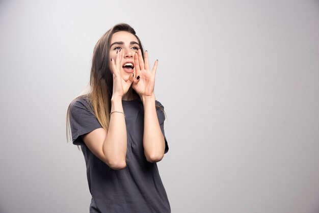 Image d'une jolie jeune femme hurlant posant isolé sur fond de mur gris.