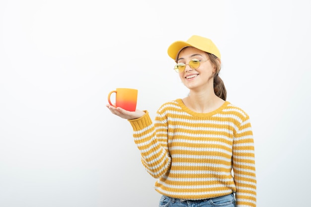 Image de jolie jeune femme à lunettes debout et tenant une tasse. Photo de haute qualité