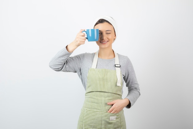 Image d'une jolie jeune femme en tablier couvrant un œil avec une tasse bleue