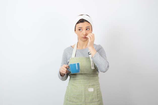 Image d'une jolie jeune femme en tablier tenant une tasse bleue