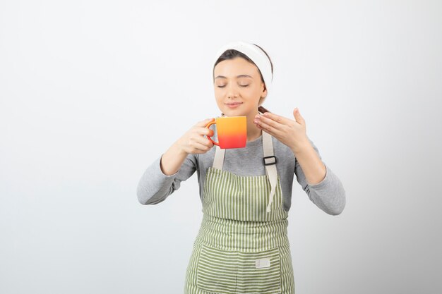 Image d'une jolie jeune femme en tablier tenant une tasse