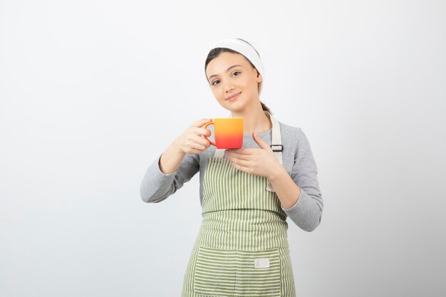 Image d'une jolie jeune femme en tablier tenant une tasse