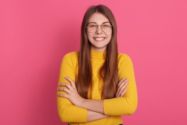 Image de joyeuse joyeuse jeune femme souriante sincèrement, regardant directement ayant les bras croisés, ayant un écart dans les dents