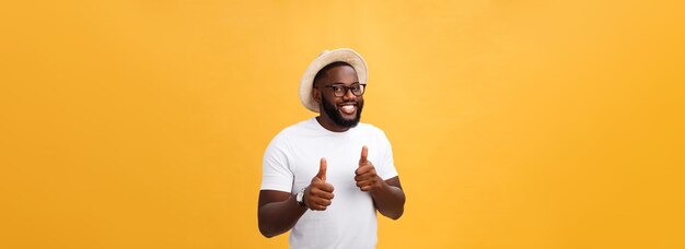 Image de joyeux jeune homme africain debout et posant sur fond jaune avec les pouces vers le haut