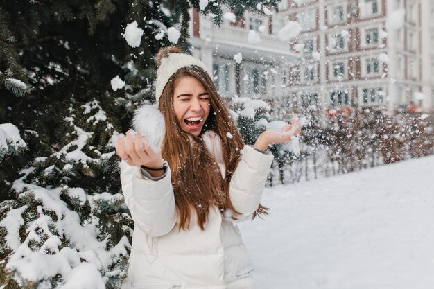 Image lumineuse excitée de joyeuse jolie femme d'hiver incroyable s'amuser avec de la neige en plein air sur la rue. Moments heureux, jouer avec des flocons de neige, profiter, émotions positives.