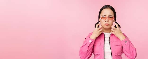 Image d'un modèle féminin adulte coréen énervé en colère serrant les poings et criant des cris indignés debout sur fond rose