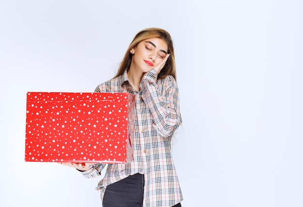 Image d'un modèle de jeune femme debout et tenant une boîte cadeau rouge.
