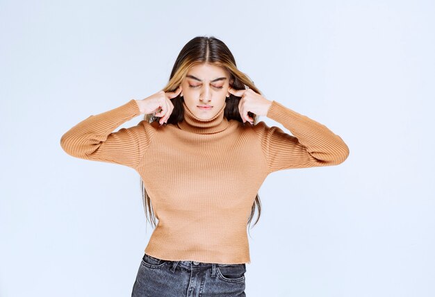 Image d'un modèle de jeune femme en pull marron couvrant les oreilles avec les doigts.