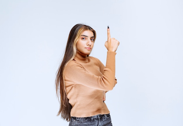 Image d'un modèle de jeune femme en pull marron debout et pointant vers le haut.