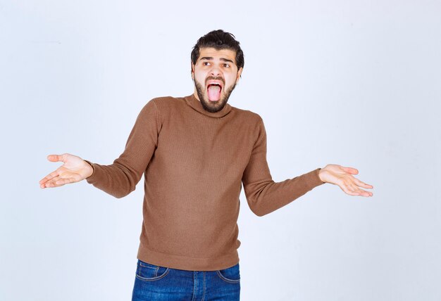 Image d'un modèle de jeune homme avec une barbe levant les paumes sur un mur blanc. photo de haute qualité