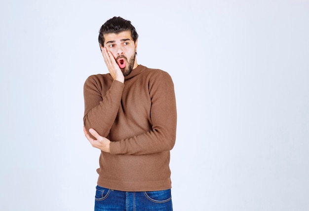 Image d'un modèle masculin en pull marron debout sur un mur blanc.