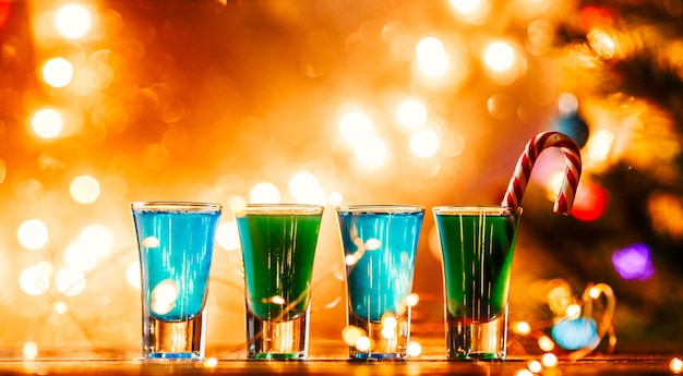 Image de noël de quatre verres à vin avec cocktail vert, bâtonnets de caramel et guirlande sur fond bleu flou du nouvel an