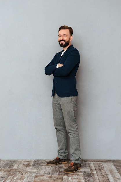 Photo gratuite image pleine longueur d'homme barbu en vêtements de travail posant avec les bras croisés et regardant la caméra sur gris