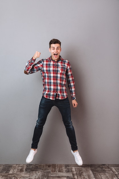 Image pleine longueur de Screaming Cheerful man in shirt and jeans jumping and looking