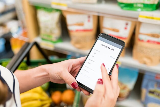 Image recadrée d'une femme vérifiant la liste de courses dans un smartphone à l'épicerie