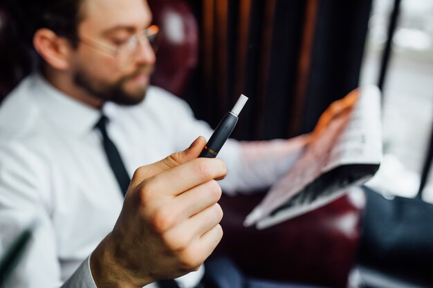 Image recadrée, homme d'affaires reposant sur un fauteuil dans une chambre de luxe, homme fumant un cigare dans sa maison.