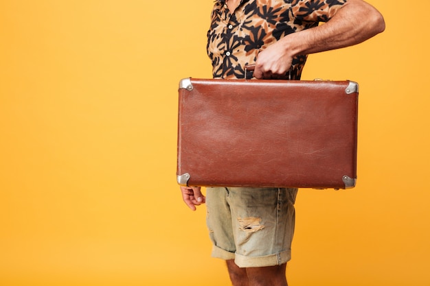 Image recadrée de jeune homme africain tenant une valise.