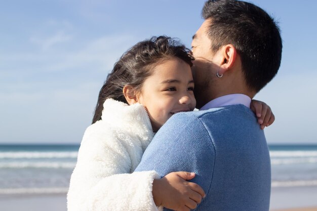 Image recadrée d'un père et d'une fille heureux sur la plage. Famille japonaise marchant, étreignant, papa portant une petite fille. Loisirs, temps en famille, concept parental