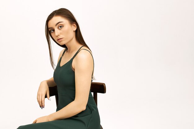 Image Studio de sérieuse belle jeune femme européenne aux longs cheveux noirs assis sur une chaise en robe d'été vert sangle.