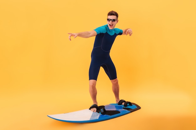 Photo gratuite image de surfeur heureux en combinaison et lunettes de soleil en utilisant une planche de surf comme sur une vague