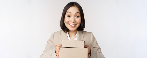 Image d'une vendeuse asiatique femme d'affaires donnant des boîtes avec commande livrée au client debout en costume sur fond blanc