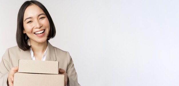 Image d'une vendeuse asiatique femme d'affaires donnant des boîtes avec commande livrée au client debout en costume sur fond blanc