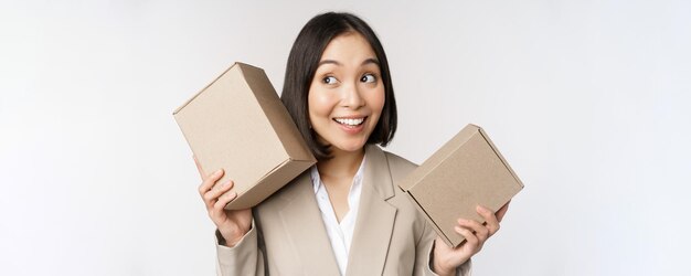 Image d'une vendeuse asiatique secouant des boîtes et devinant ce qu'il y a à l'intérieur souriant pensif debout sur fond blanc